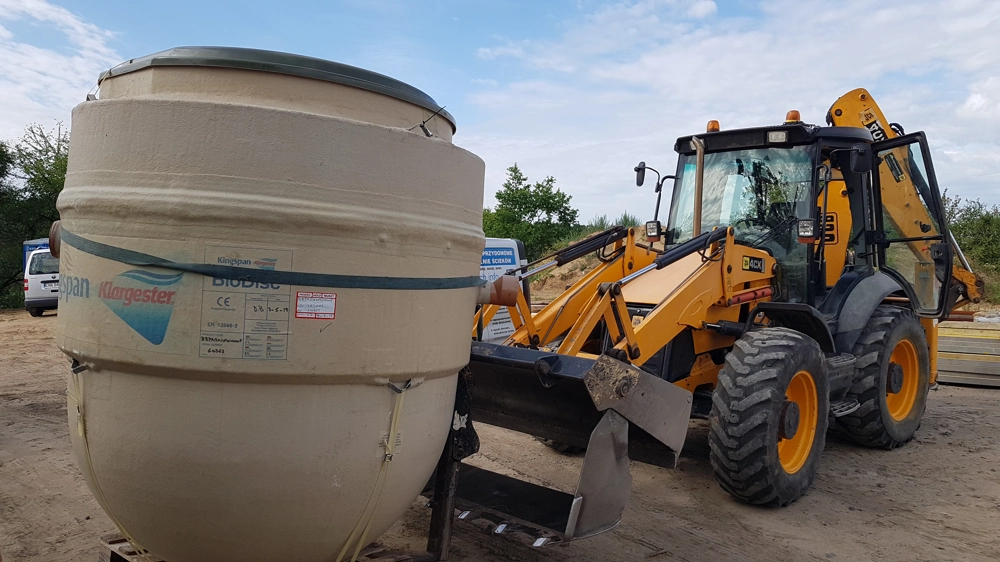 Plastikowy zbiornik na szambo obok koparki, prace ziemne przy instalacji szamba