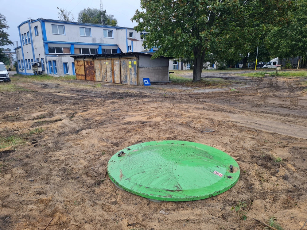 Zielona pokrywa szamba betonowego na odsłoniętym podłożu podczas prac ziemnych