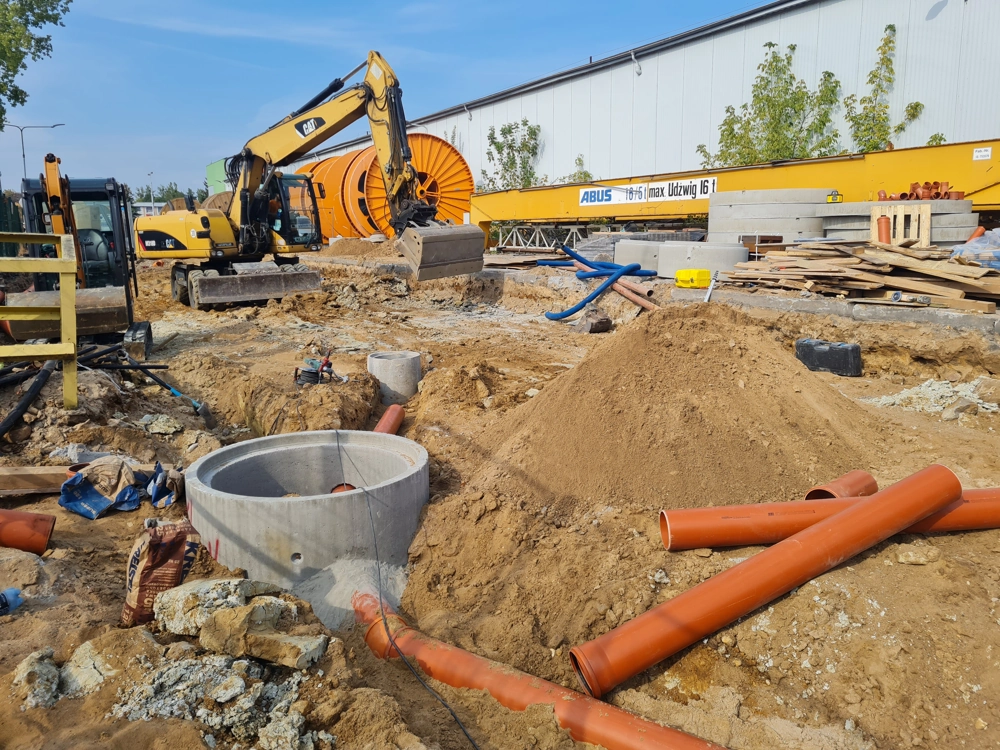 Prace ziemne przy instalacji betonowej studni rewizyjnej i układaniu pomarańczowych rur kanalizacyjnych