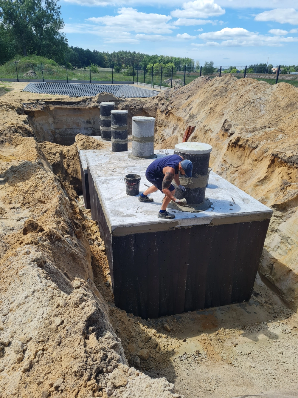 Przydomowa oczyszczalnia ścieków instalowana w wykopie, pracownik zabezpiecza betonowy zbiornik