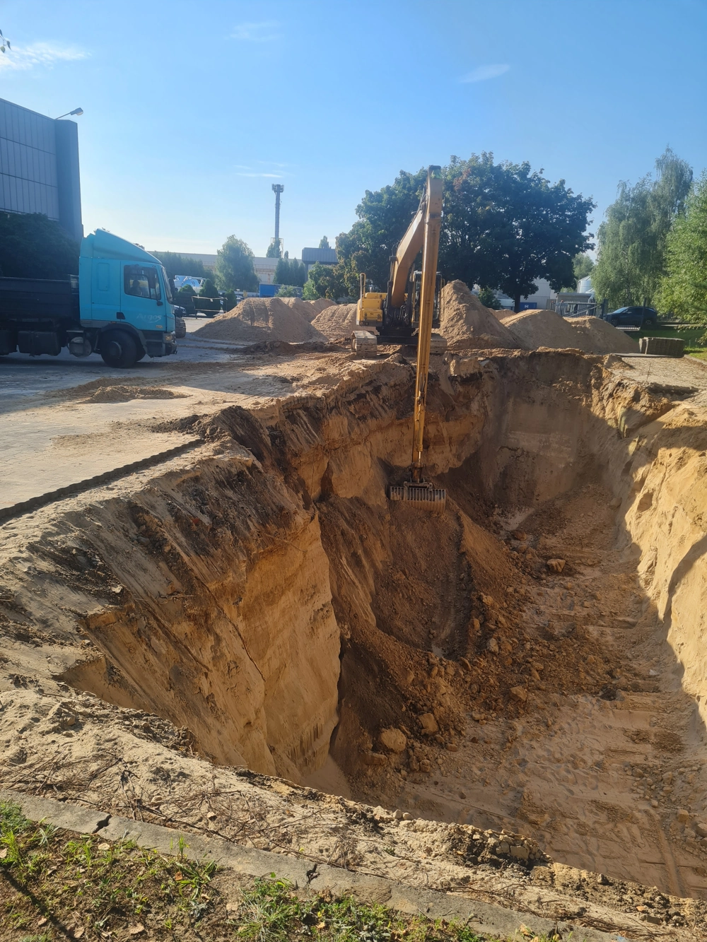 Duży wykop ziemny z koparką i ciężarówką na placu budowy – prace ziemne