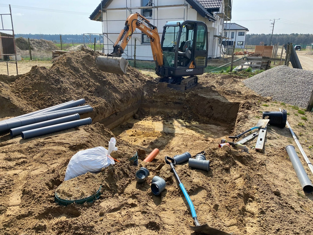 Prace ziemne pod przydomową oczyszczalnię ścieków z koparką i rurami PVC