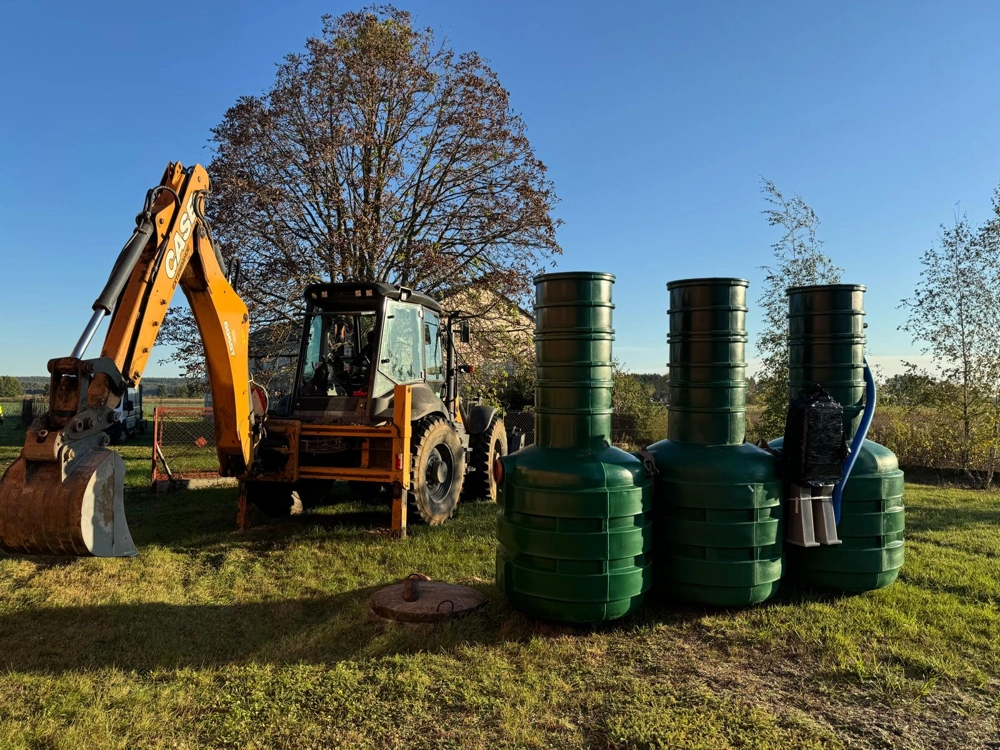 Trzy zielone moduły przydomowej oczyszczalni ścieków obok koparki