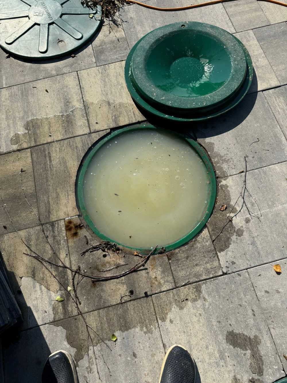 Otwarty właz przydomowej oczyszczalni ścieków z mętną wodą