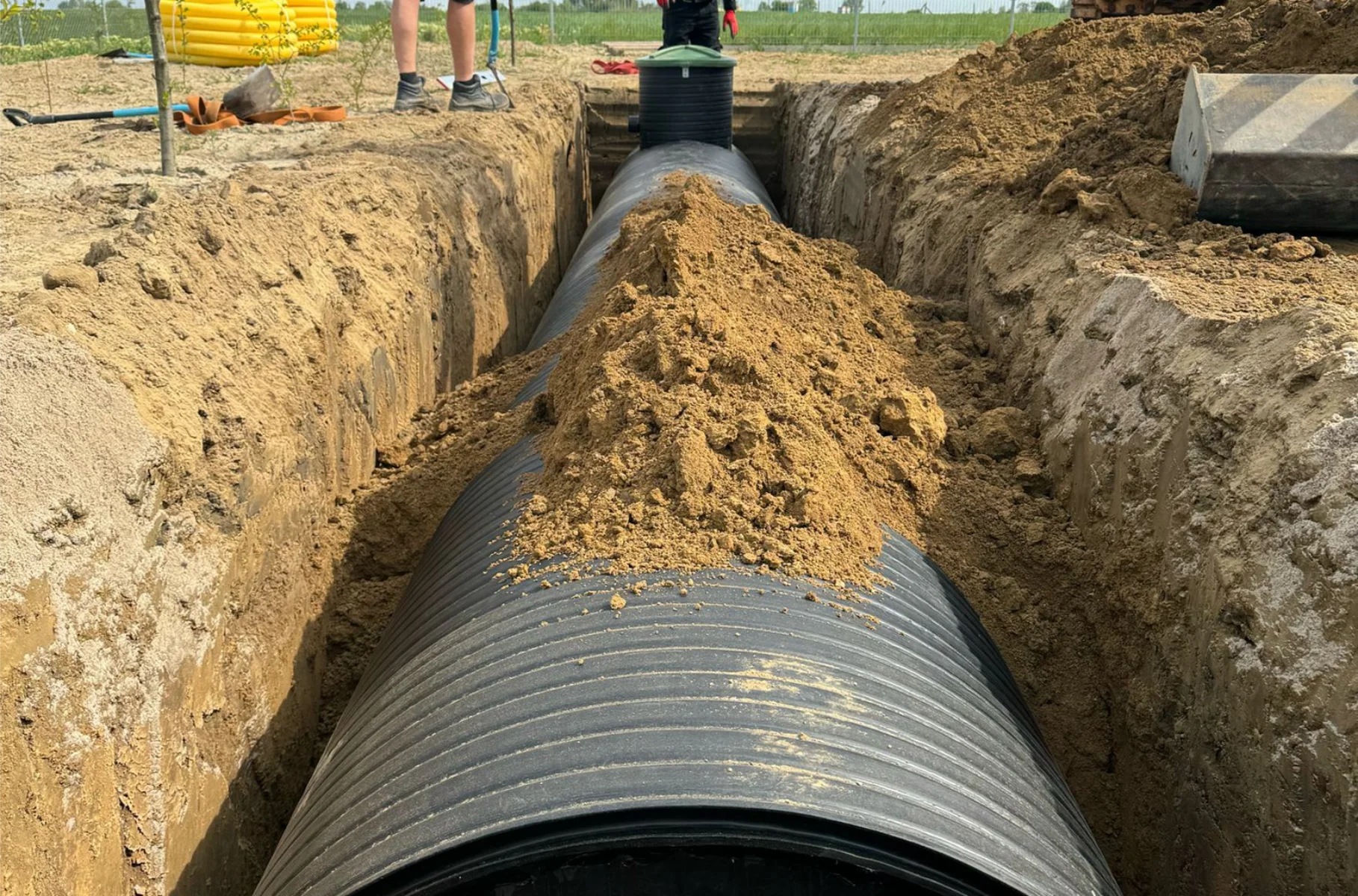 Układanie dużej rury karbowanej w wykopie podczas prac ziemnych