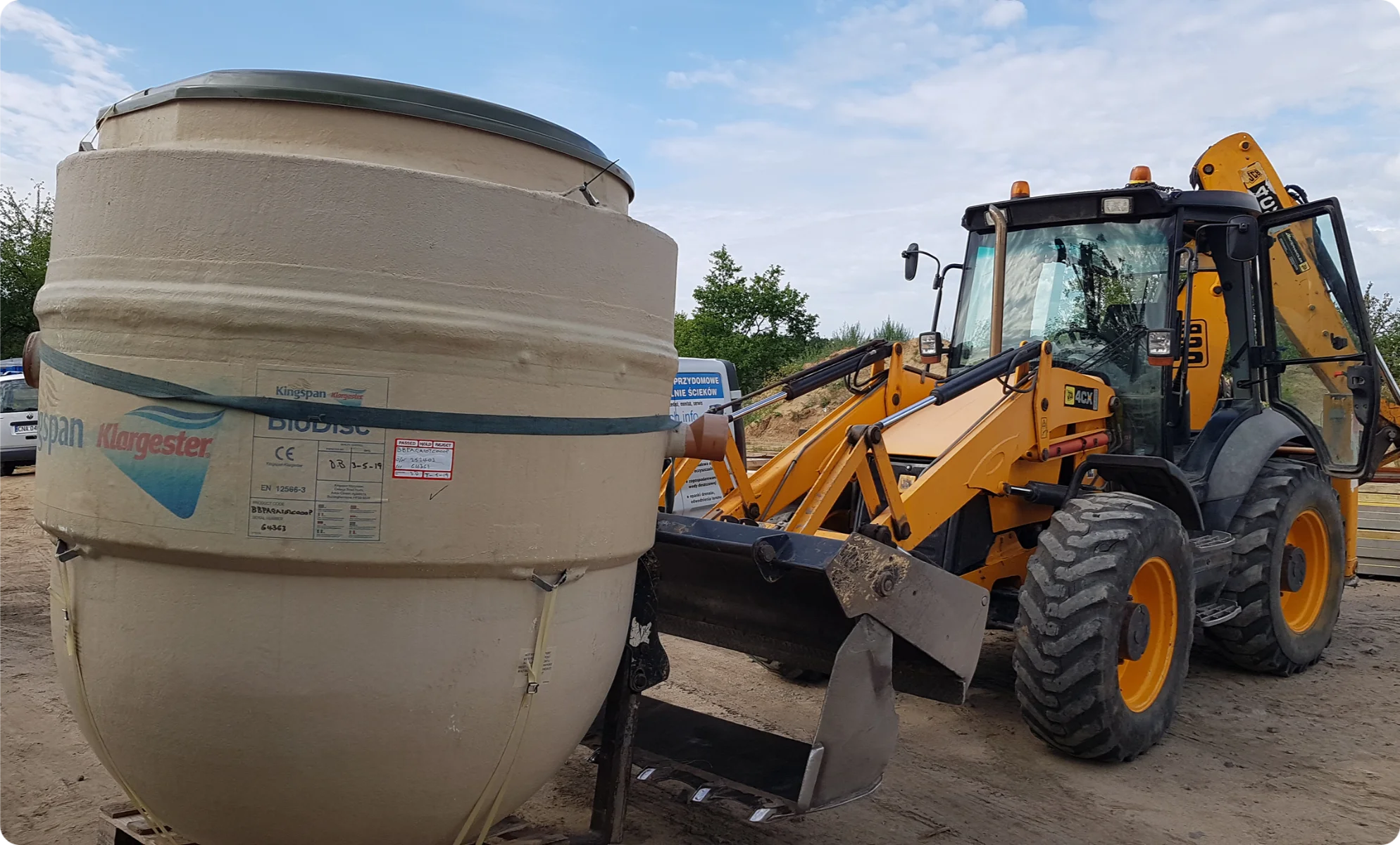 Koparka ładowarka obok zbiornika szamba na budowie