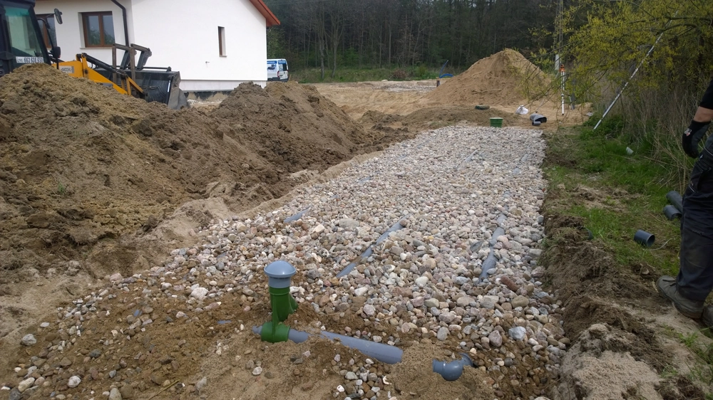 Rury drenarskie i zielony odpowietrznik osadzone na podsypce żwirowej podczas prac ziemnych przy budowie przydomowej oczyszczalni ścieków