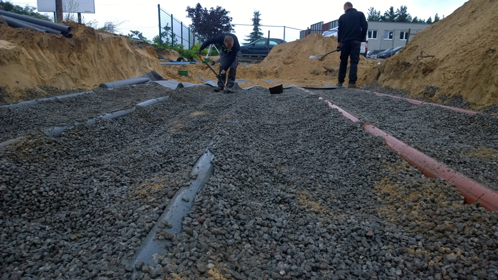 Ekipa wykonuje drenaż w żwirowanym wykopie